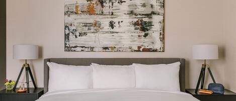Een hotelkamer met een groot bed, twee nachtkastjes met lampen en een groot abstract schilderij aan de muur.