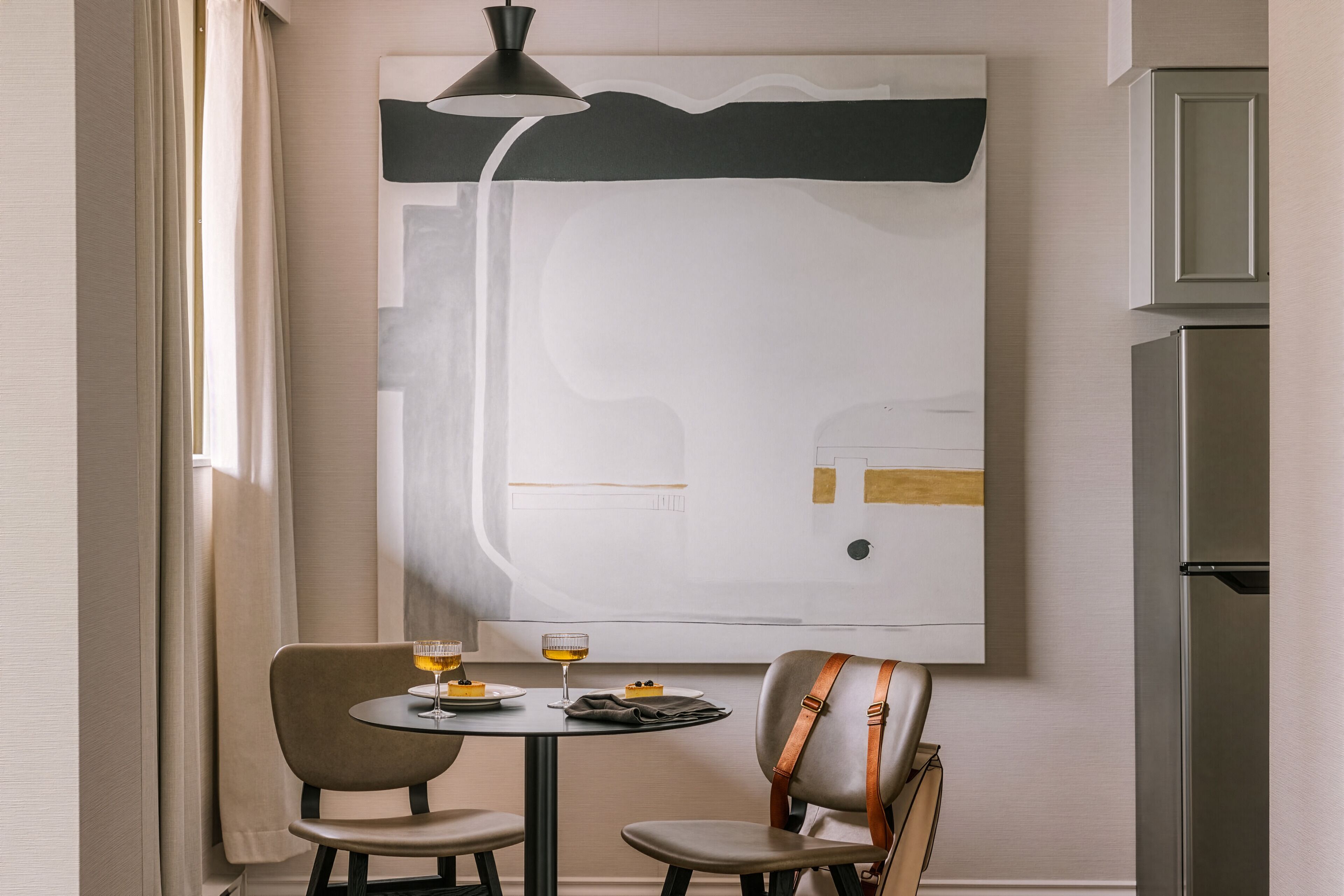 Un comedor moderno con un cuadro abstracto grande, una mesa con dos sillas y un refrigerador al fondo.