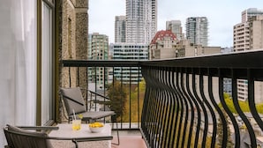 A balcony with a table and chairs, a view of a cityscape with tall buildings, and a decorative railing. - The Sunset Hotel West End (Vancouver)
