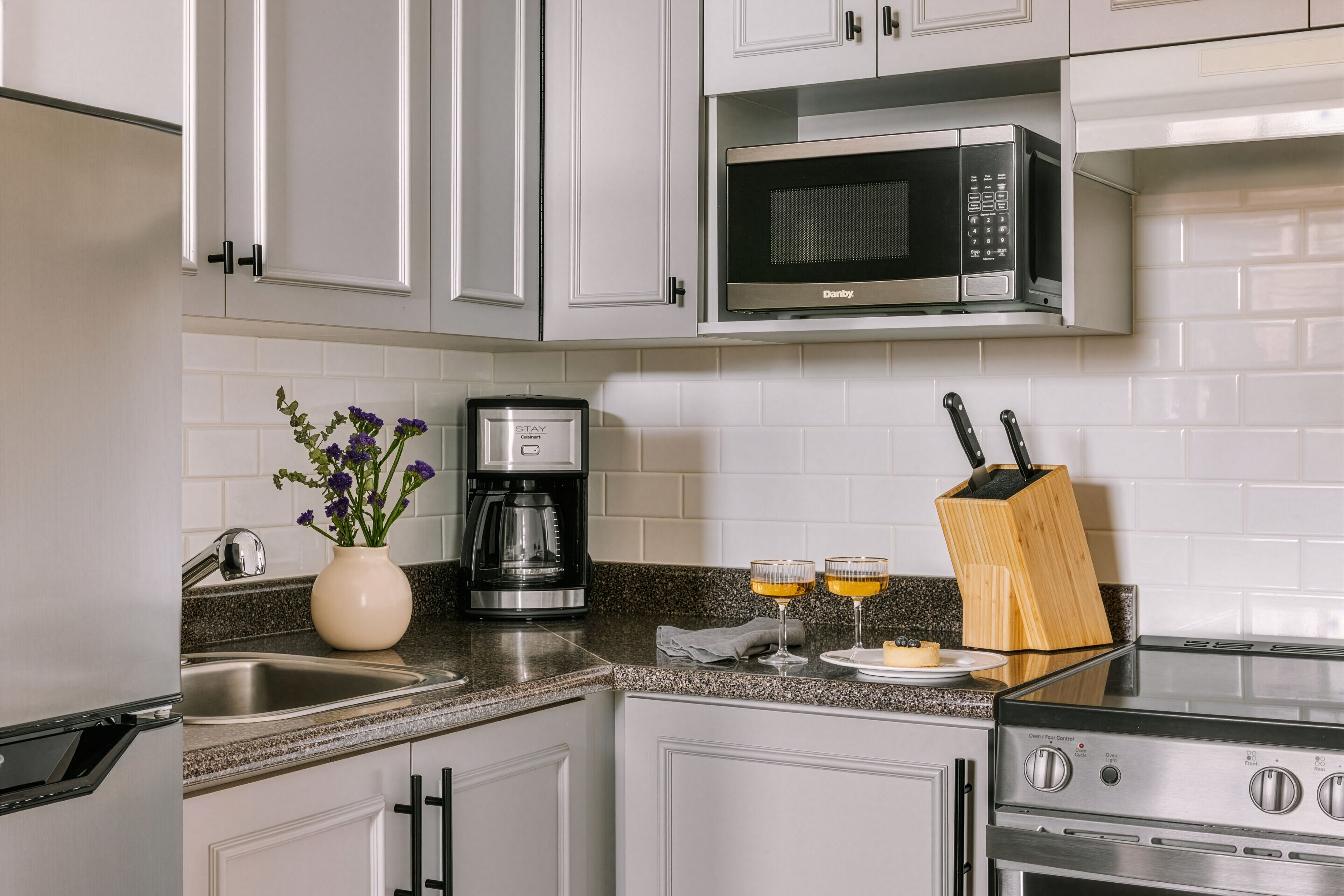A modern kitchen with white cabinets, a stainless steel microwave, a coffee maker, and a knife block.