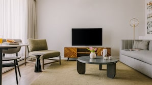 A modern living room with a sofa, a coffee table, a TV, and a dining area with a table and chairs. - The Sunset Hotel West End (Vancouver)