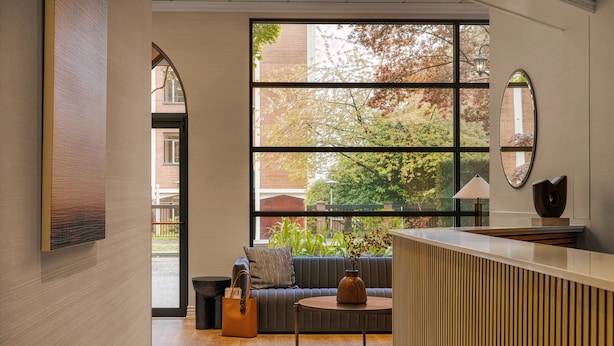 A modern lobby with a large window, a sofa, a small table, and a reception desk. - The Sunset Hotel West End (Vancouver)