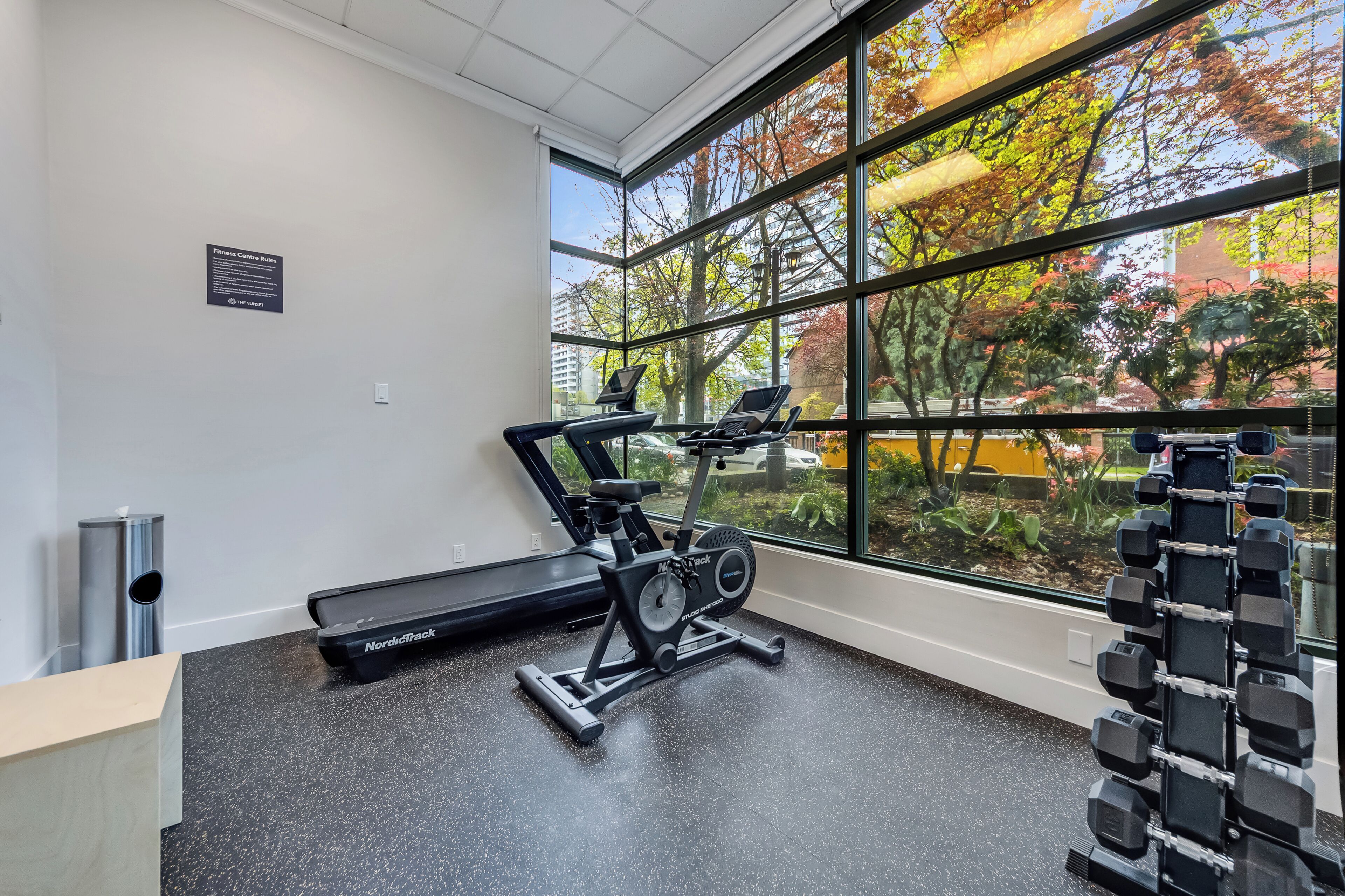 A gym with exercise equipment, a window with a view of trees, and a wall-mounted sign.