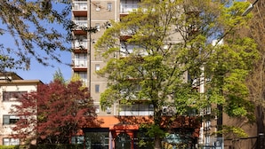 A multi-story residential building with balconies, a tree in front, and a clear blue sky. - The Sunset Hotel West End (Vancouver)