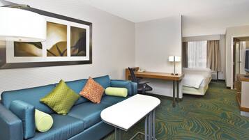 A hotel room with a blue sofa, a small table, a desk, a bed, and a mirror.