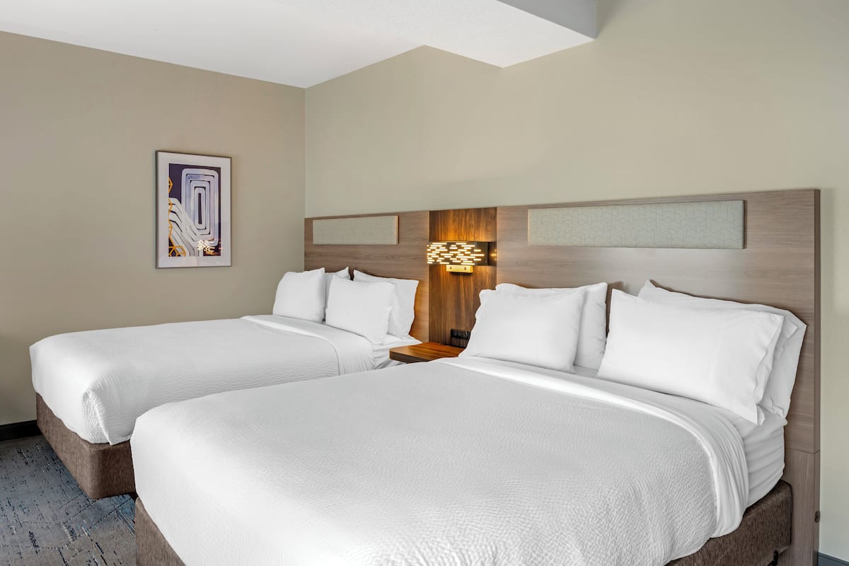 A hotel room with two beds, a headboard with a light fixture, and a framed artwork on the wall.