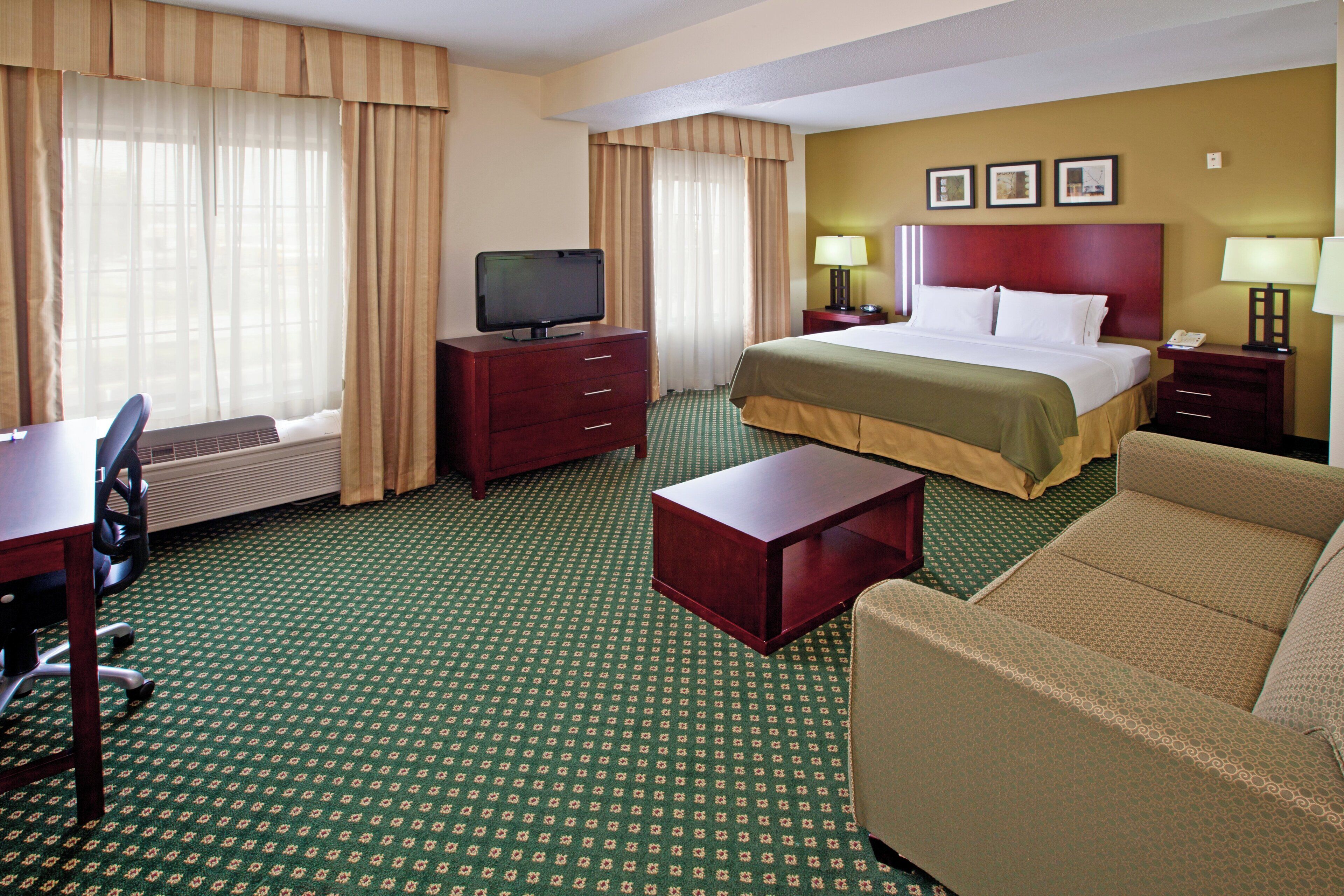 A hotel room with a bed, a desk with a chair, a television, a sofa, and a small table.