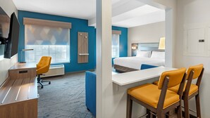 Quarto de hotel com uma escrivaninha, uma cadeira, uma cama e uma janela com persianas.
