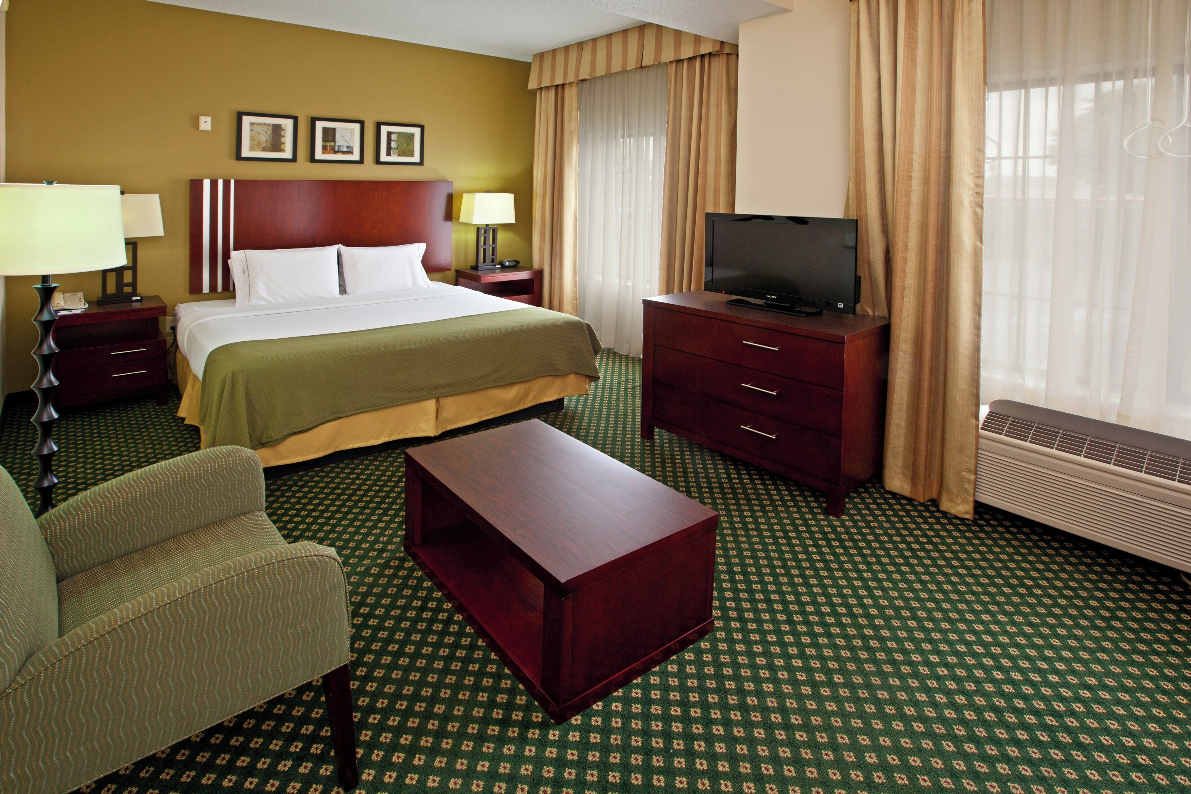 A hotel room with a bed, a television on a dresser, a desk, and a chair.