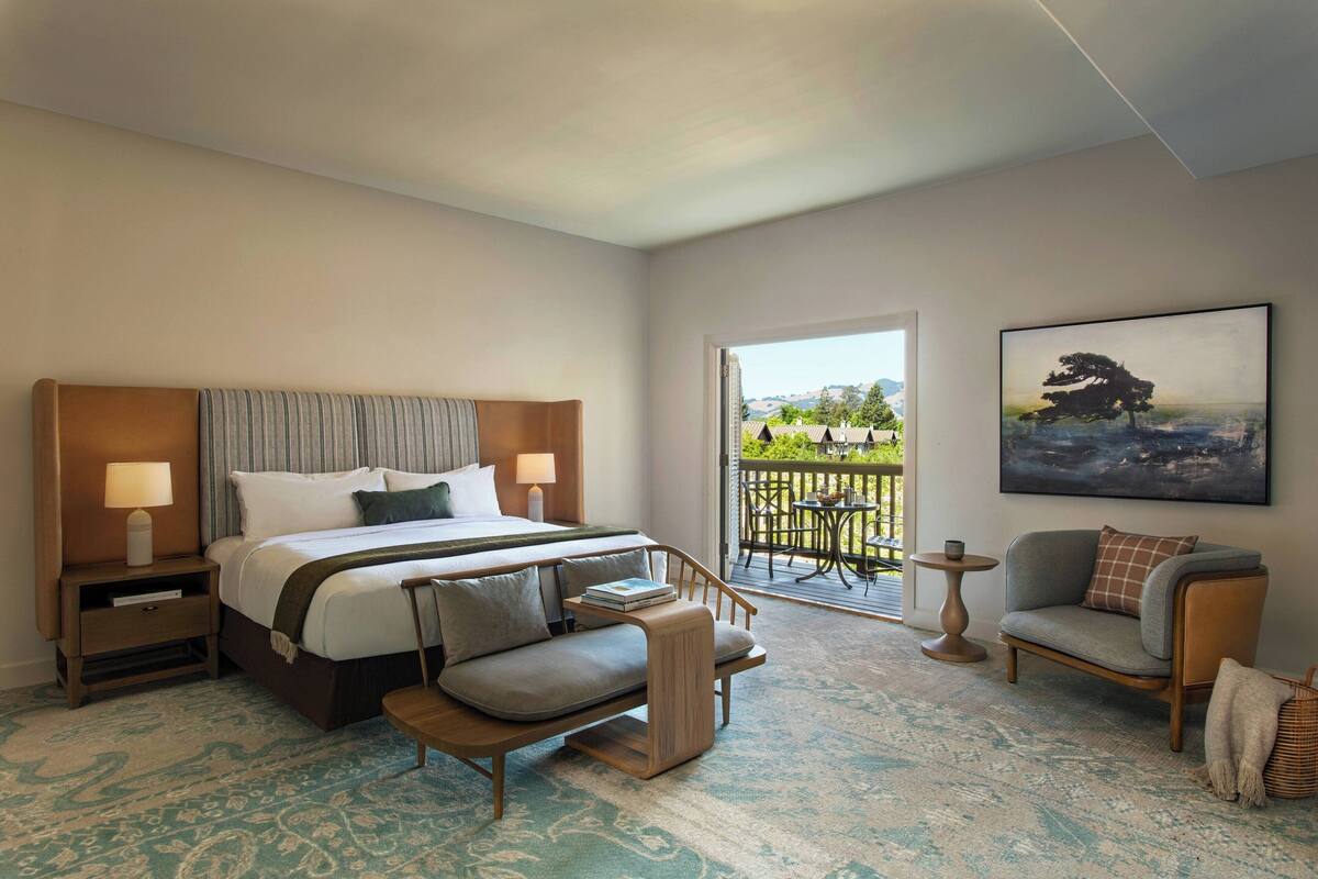 Hotelkamer met een bed, nachtkastjes, een bank, een stoel, een klein tafeltje en een balkon met uitzicht.