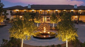 Un hotel con un patio central que presenta una escultura esférica, rodeado de árboles y un sendero pavimentado.