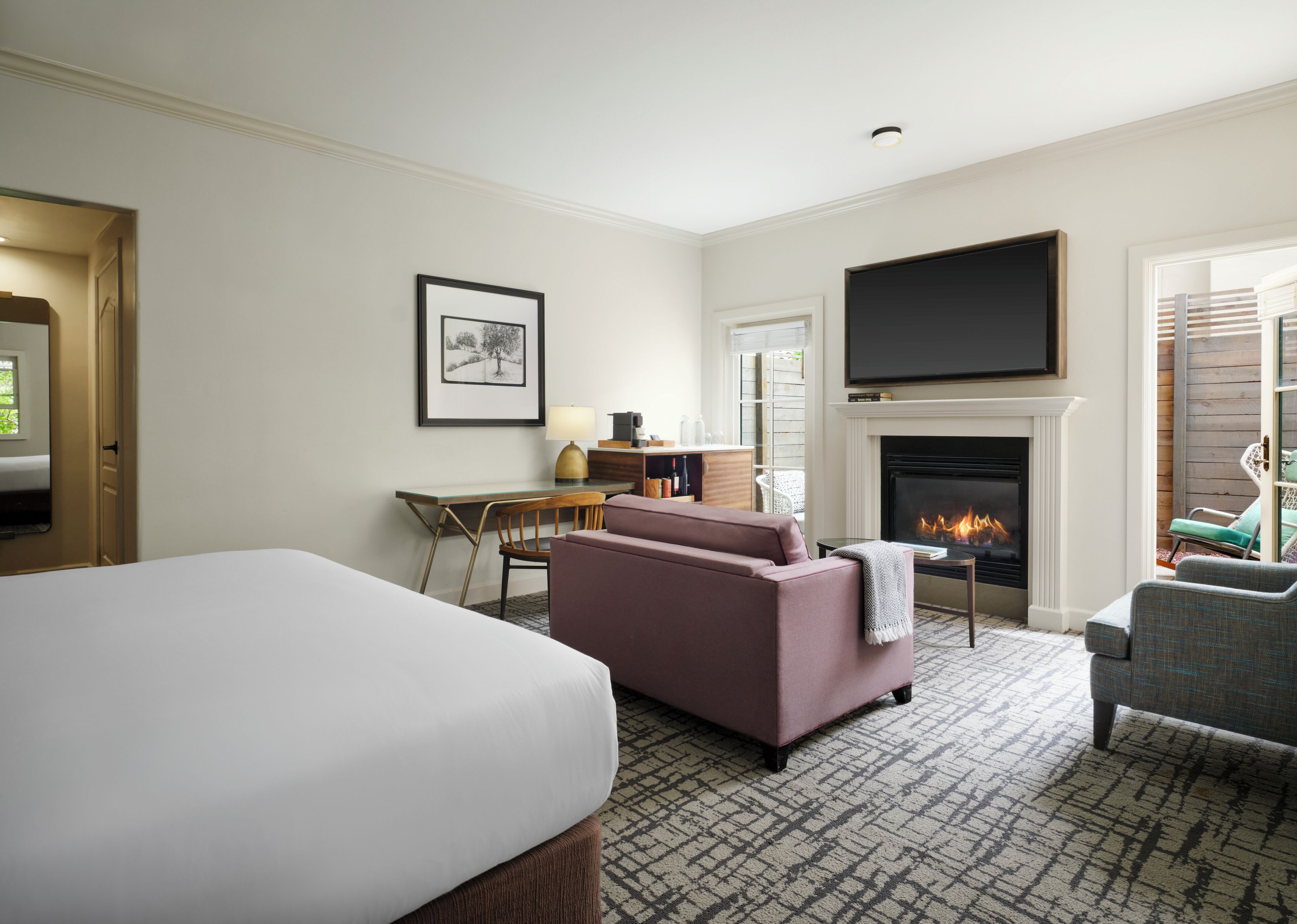 A hotel room with a bed, a sofa, a desk with a chair, a fireplace, and a TV mounted above it.