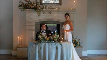 A wedding reception with a fireplace, floral arrangements, and candles.