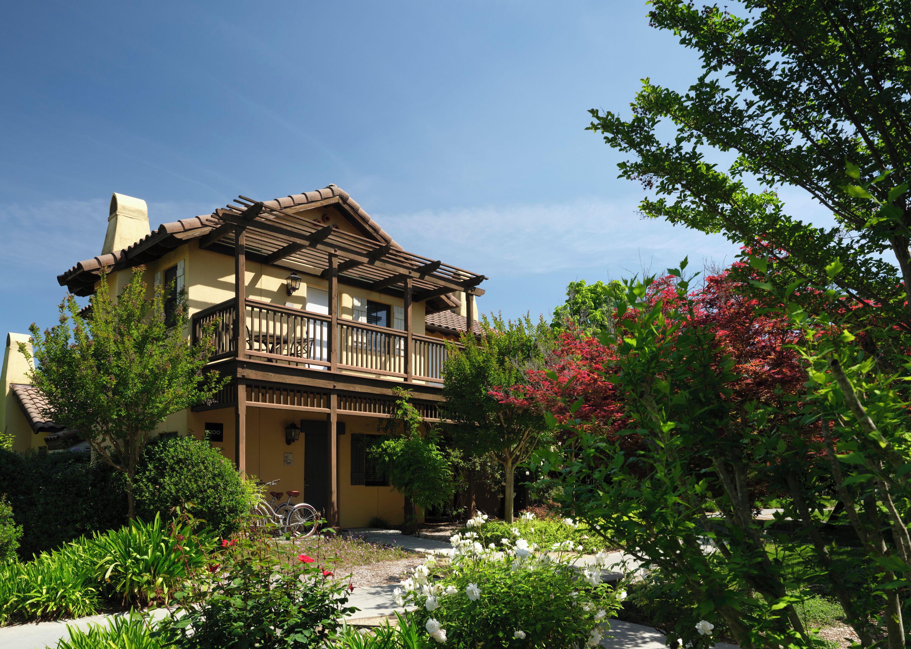 A two-story building with a balcony, surrounded by lush greenery and flowering plants.