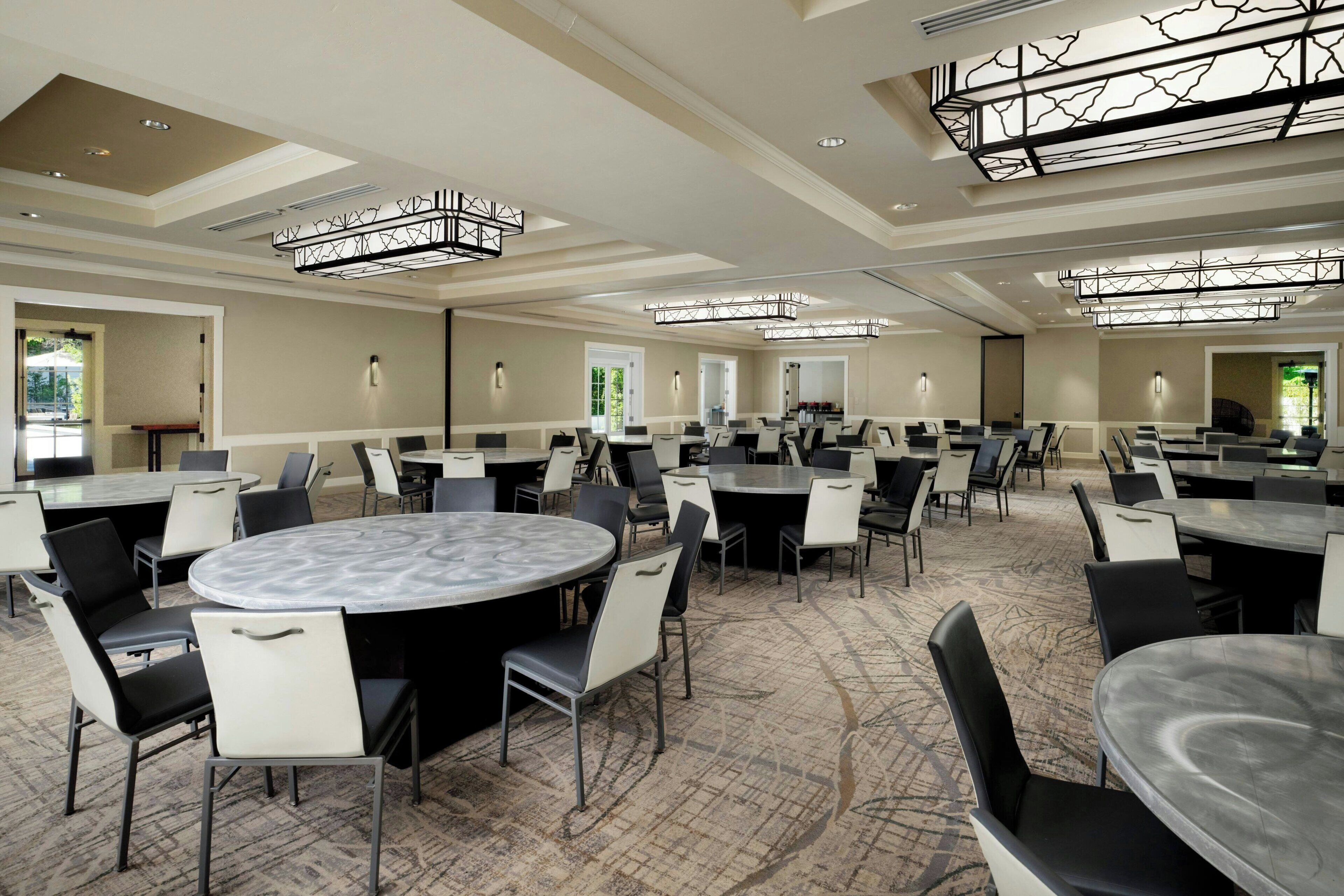 A conference room with multiple tables and chairs, high ceilings with unique lighting fixtures, and a carpeted floor.