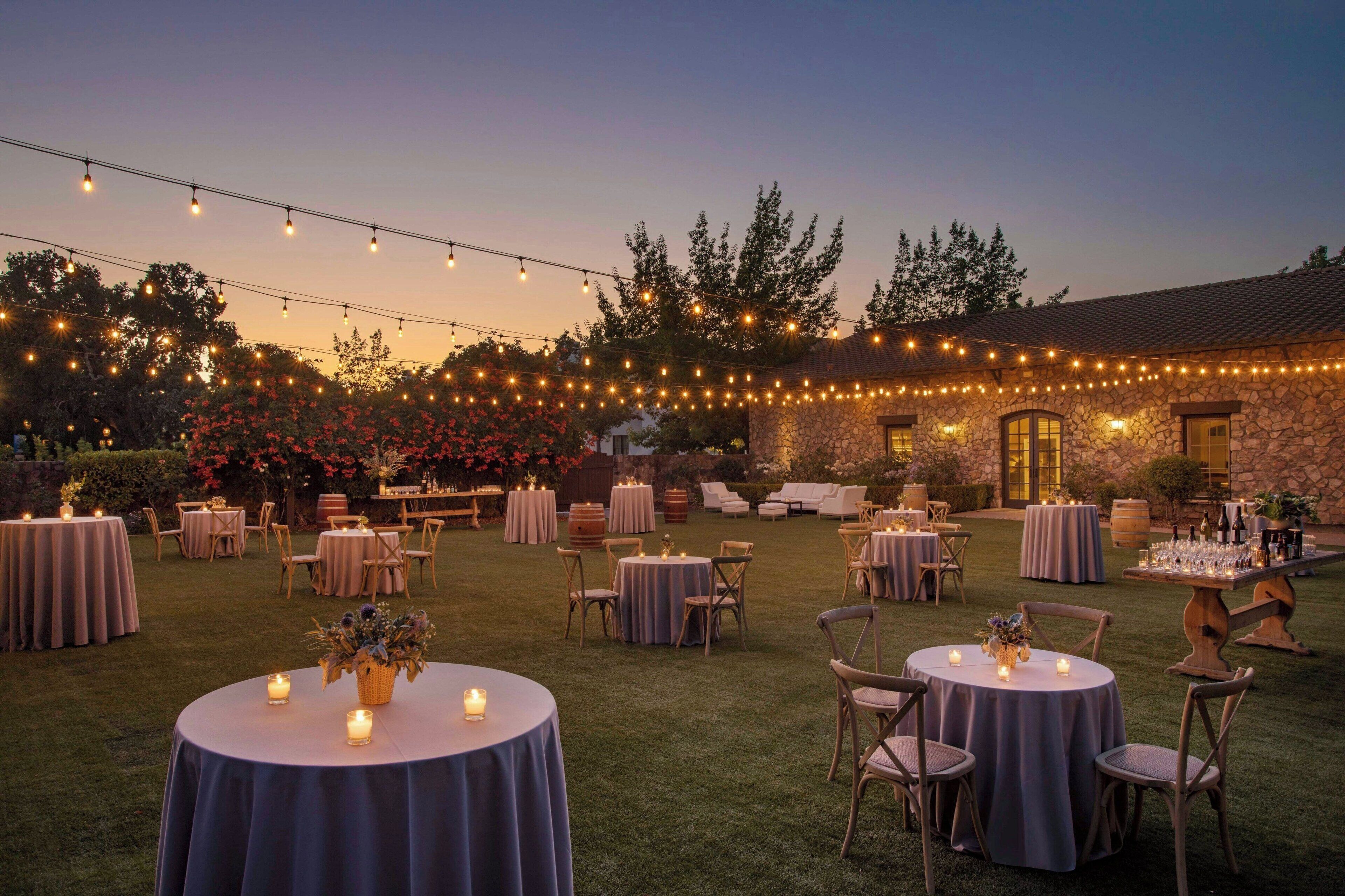 An outdoor event space with round tables, chairs, and string lights.