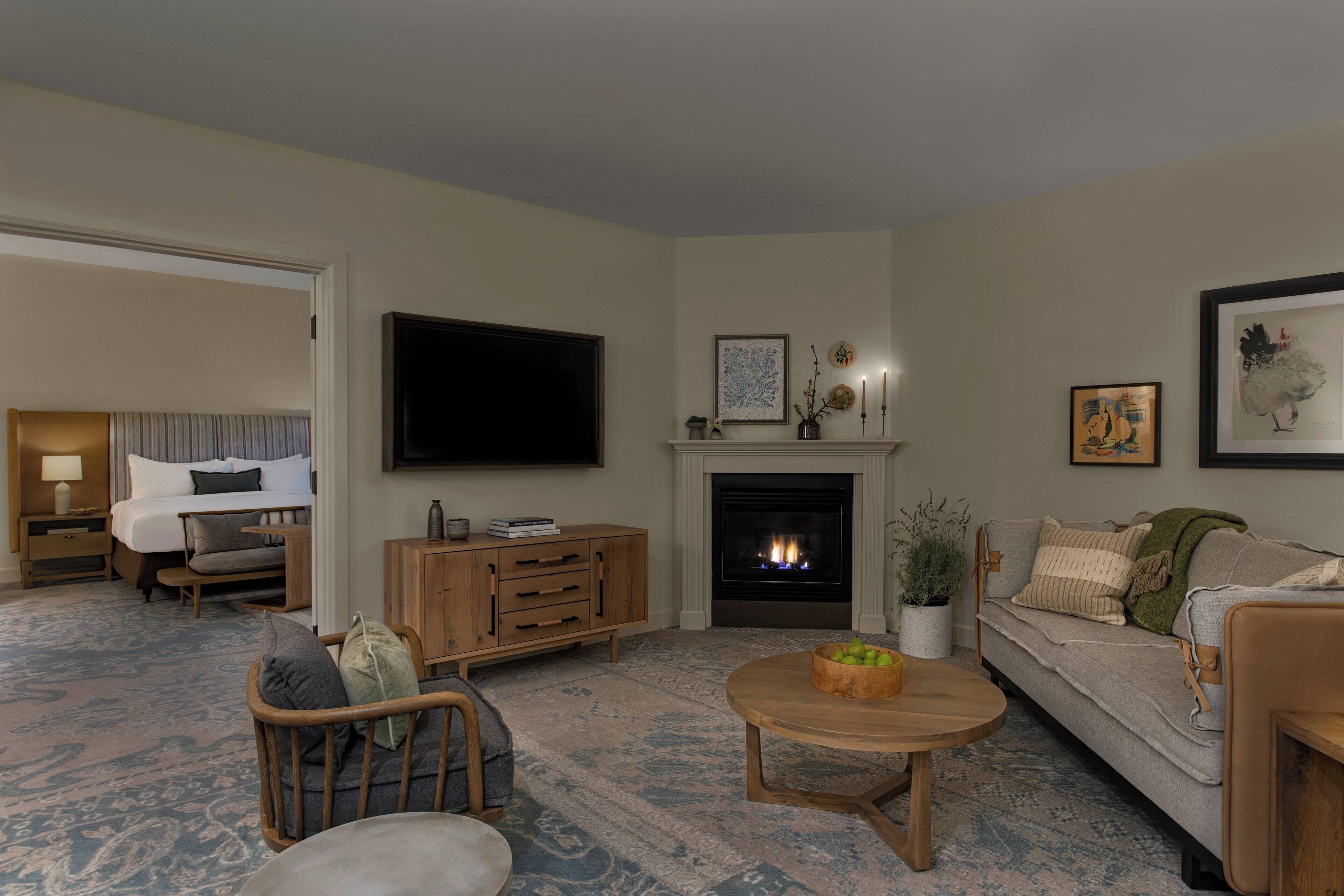A living room with a fireplace, a television, a sofa, a coffee table, and a bed with a headboard.
