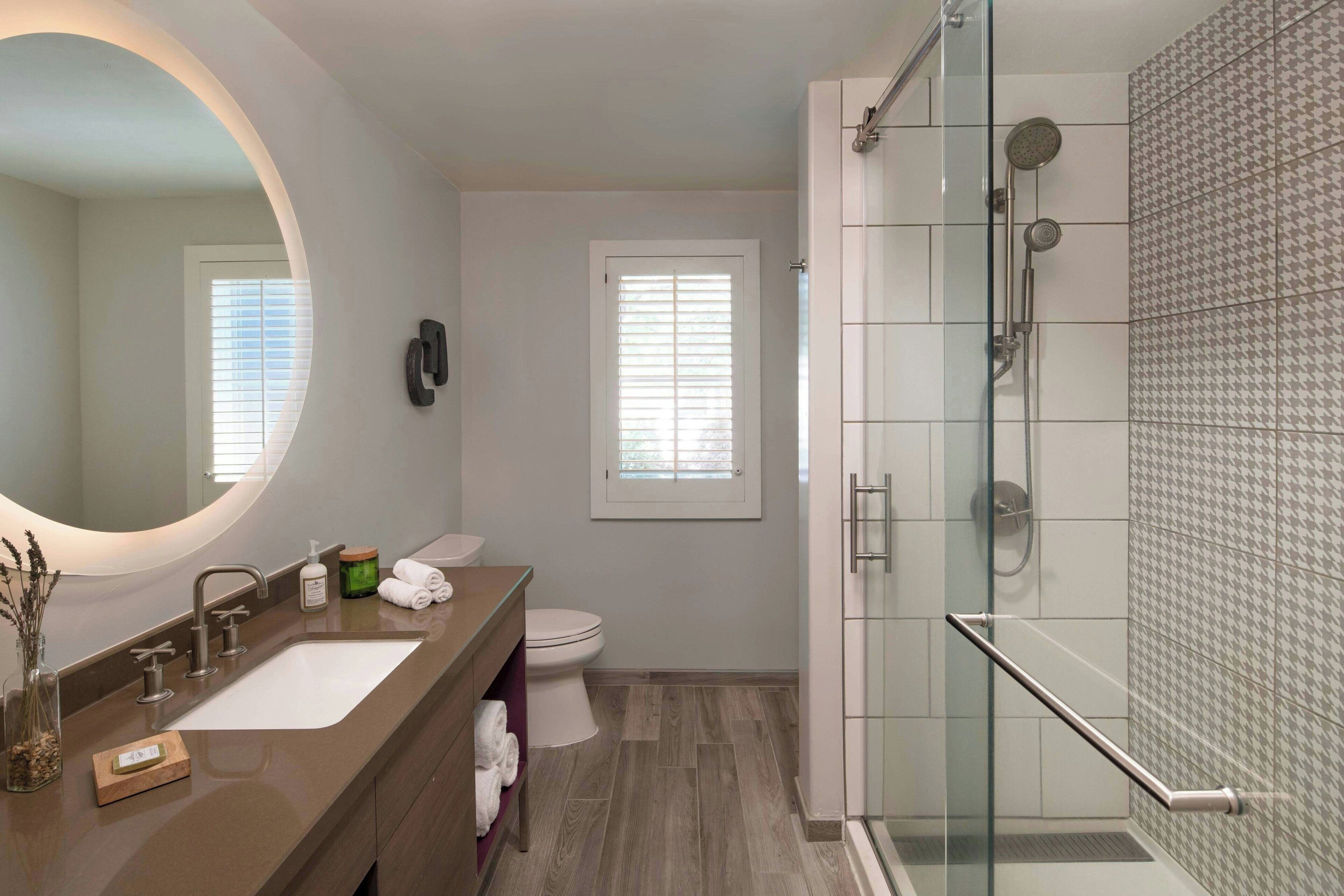 A modern bathroom with a glass-enclosed shower, a large mirror, and a vanity with a sink and toiletries.