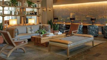 A modern hotel lobby with a sofa, chairs, a coffee table, and a reception desk.