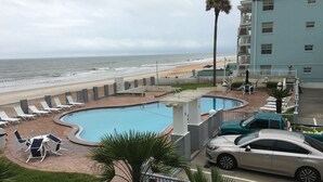Zona de piscina amb gandules, un cotxe i un edifici amb un balcó davant de la platja.