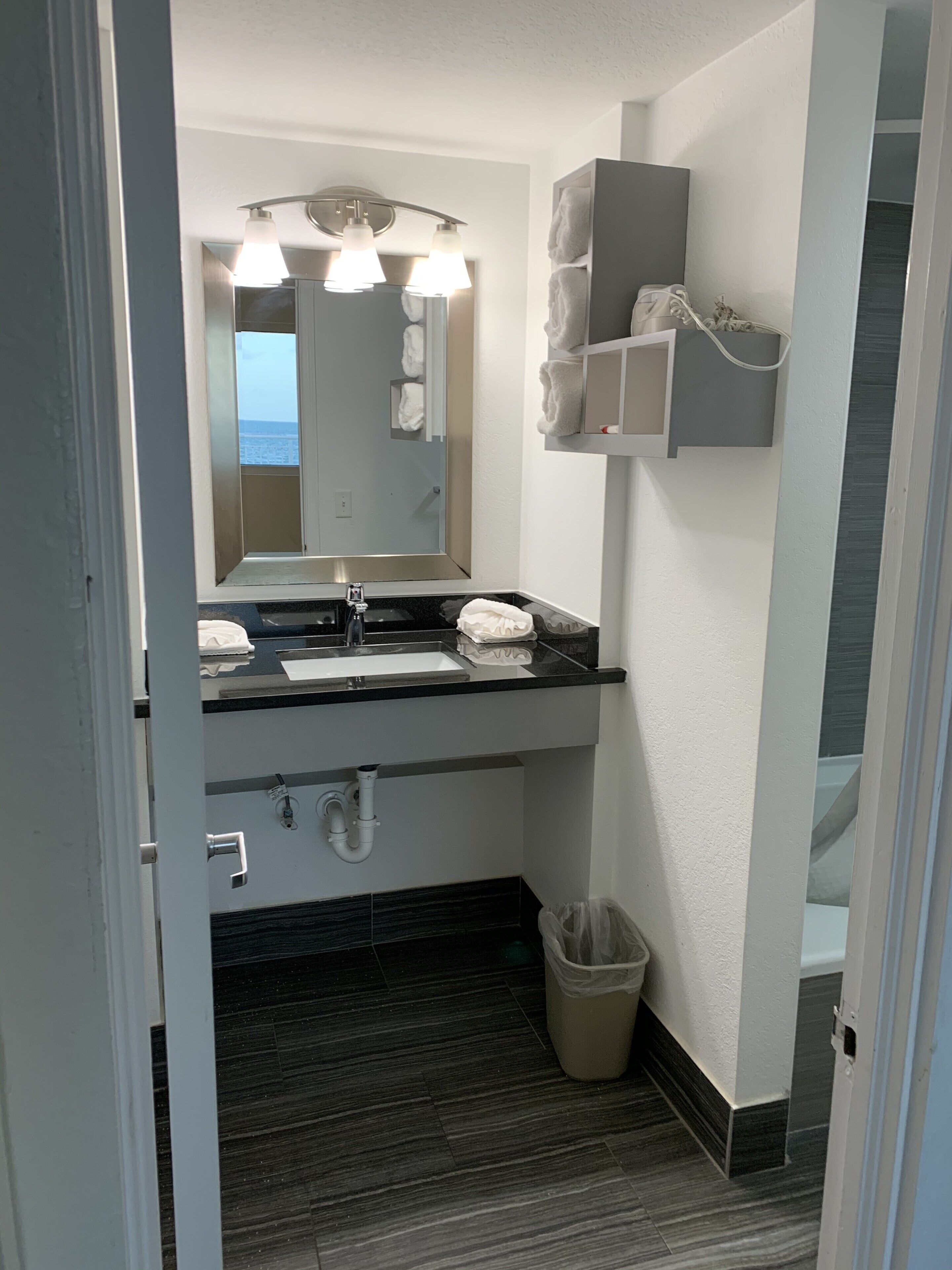 A modern bathroom with a black countertop, a large mirror, and a towel rack.