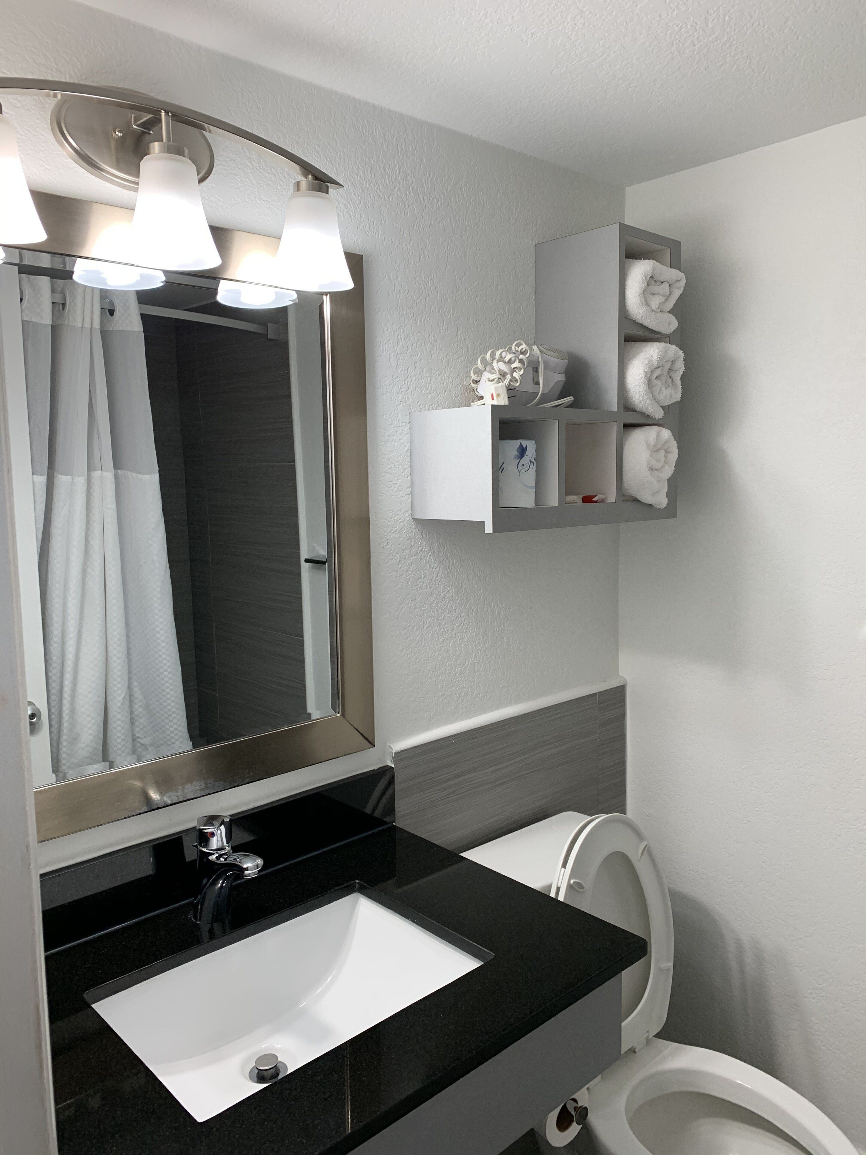 Une salle de bain moderne avec un lavabo noir, des toilettes blanches et un miroir avec éclairage intégré. Un porte-serviettes avec des serviettes est placé au-dessus des toilettes.