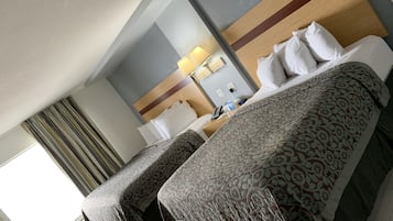 A hotel room with two beds, a desk, a lamp, and a window with curtains.
