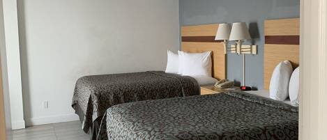 A hotel room with two beds, a nightstand, a lamp, and a wall-mounted phone.