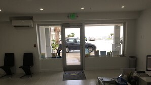 Una zona d'entrada amb un taulell de recepció, cadires, un senyal d'emergència i vistes a cotxes aparcats a l'exterior.