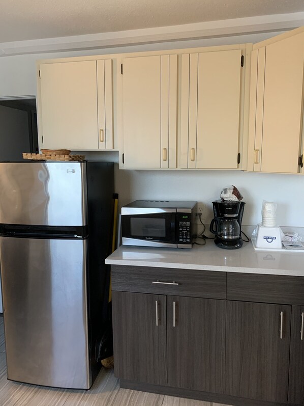 Una cocina con un refrigerador de acero inoxidable, un microondas, una cafetera y armarios de madera.
