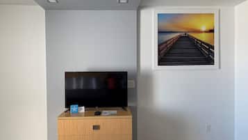 A room with a wooden dresser, a flat-screen TV, and a framed sunset picture on the wall.