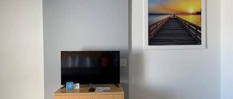 Una habitación con un aparador de madera, un televisor de pantalla plana y un cuadro en el muro con una imagen de atardecer.