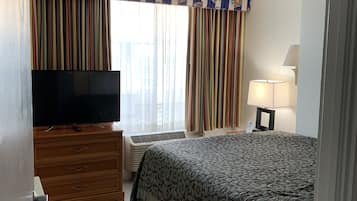 Una habitación de hotel con una cama, un televisor sobre un aparador de madera, una lámpara y cortinas.