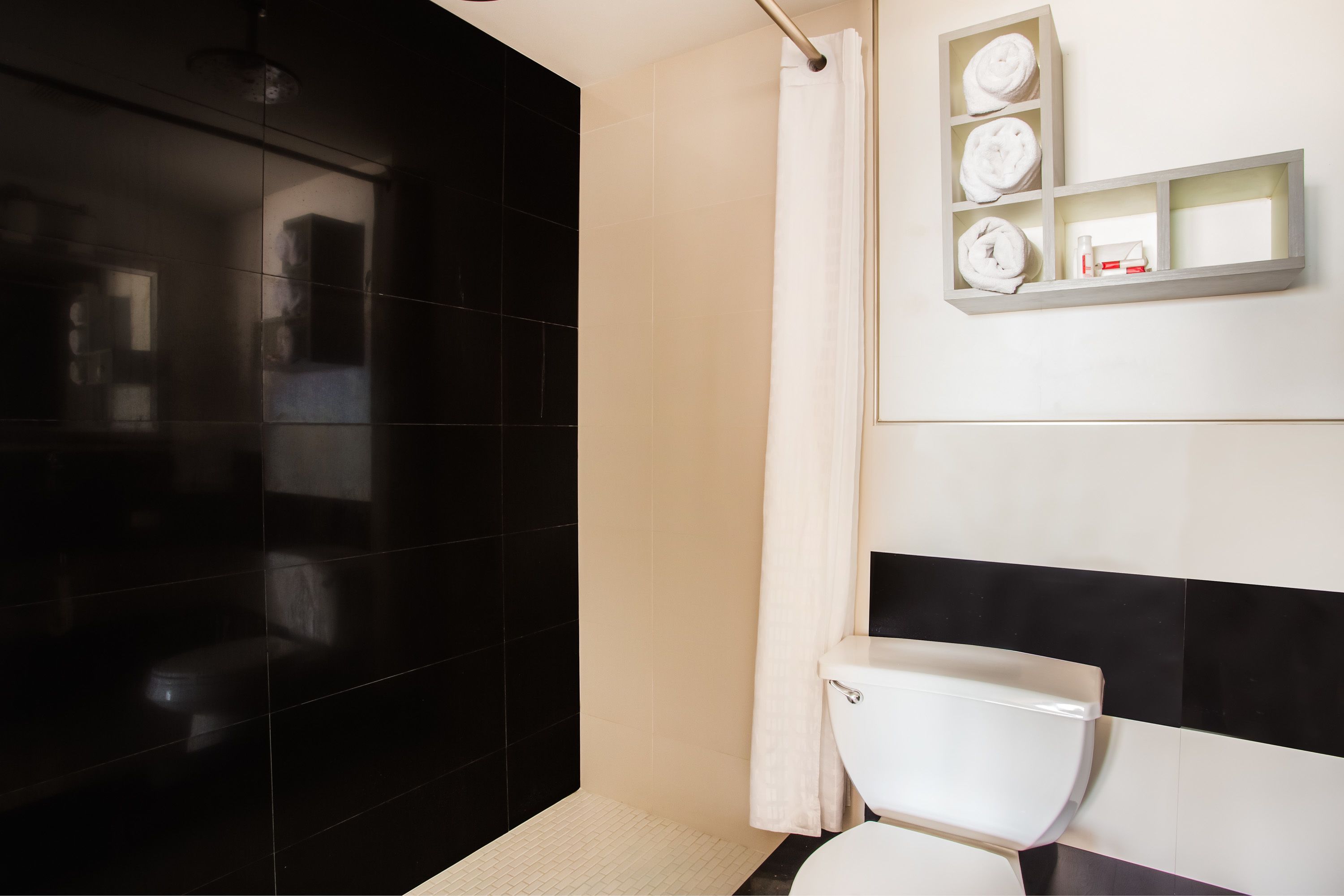 Une salle de bain moderne avec un mur recouvert de carreaux noirs et blancs, des toilettes blanches et une étagère où sont posées des serviettes et des articles de toilette.