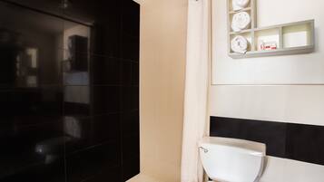 Une salle de bain moderne avec un mur recouvert de carreaux noirs et blancs, des toilettes blanches et une étagère où sont posées des serviettes et des articles de toilette.