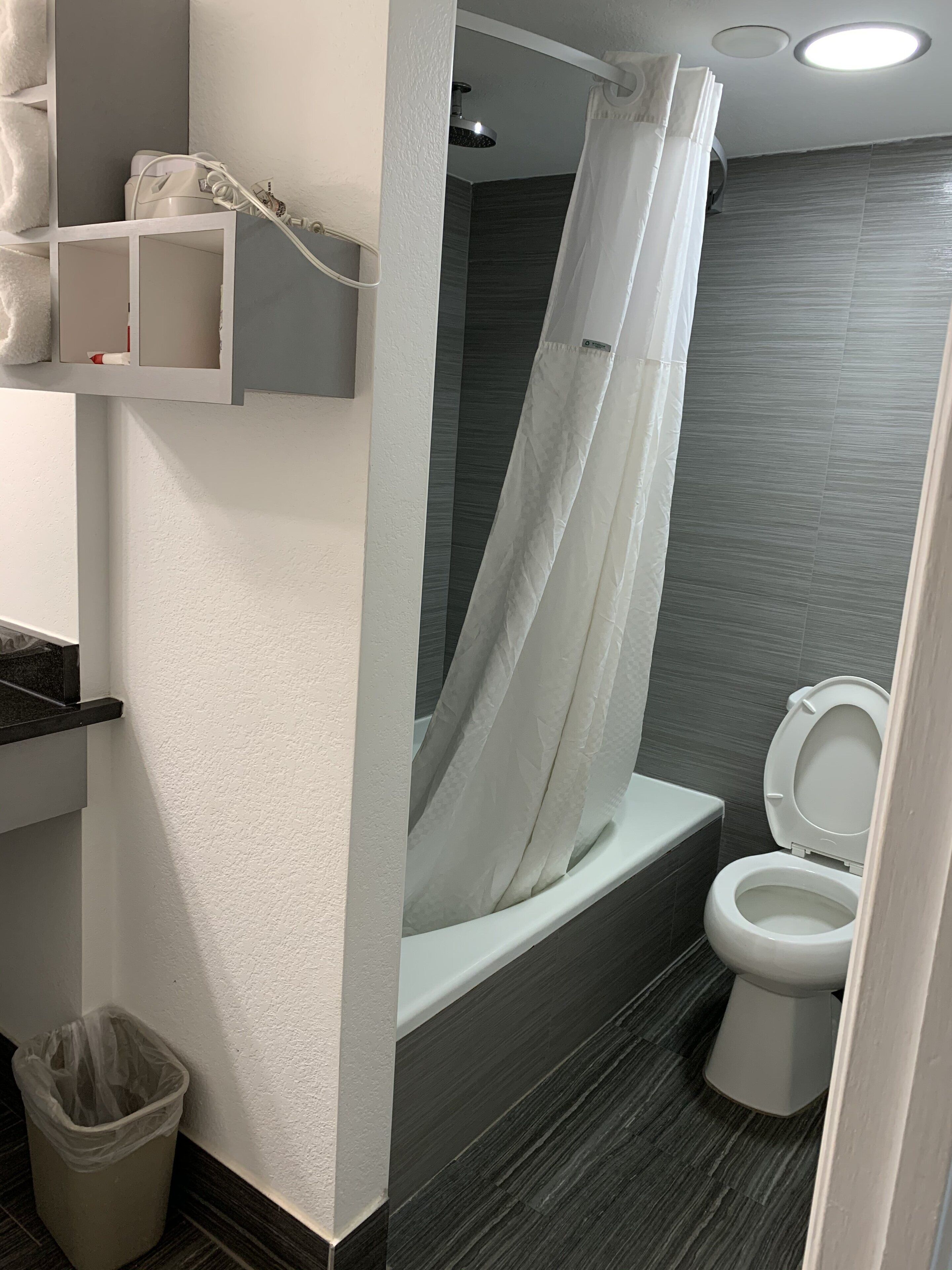 Un baño moderno con ducha, inodoro y cubo de basura.