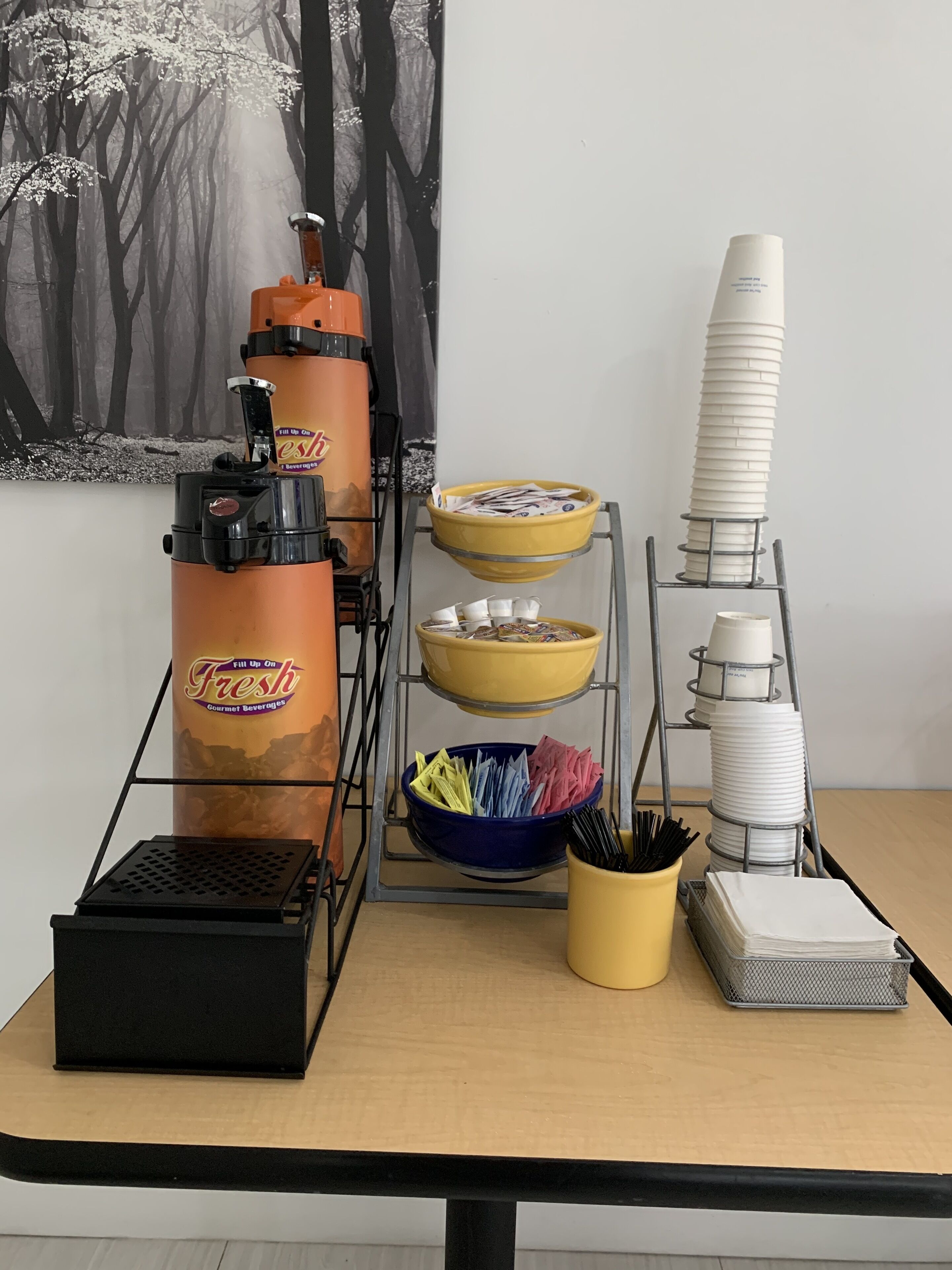 A beverage station with a coffee machine, cups, napkins, and a menu holder.