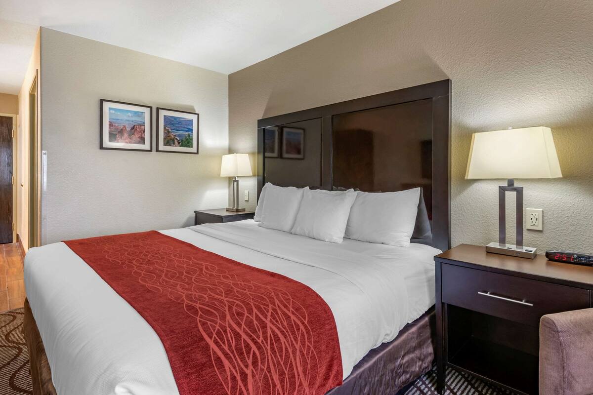 A hotel room with a large bed, a nightstand with a lamp, a dresser, and two framed pictures on the wall.
