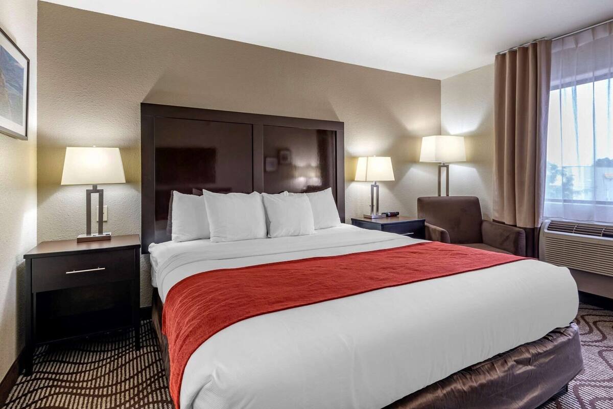 A hotel room with a large bed, two bedside tables with lamps, a chair, and a window with curtains.