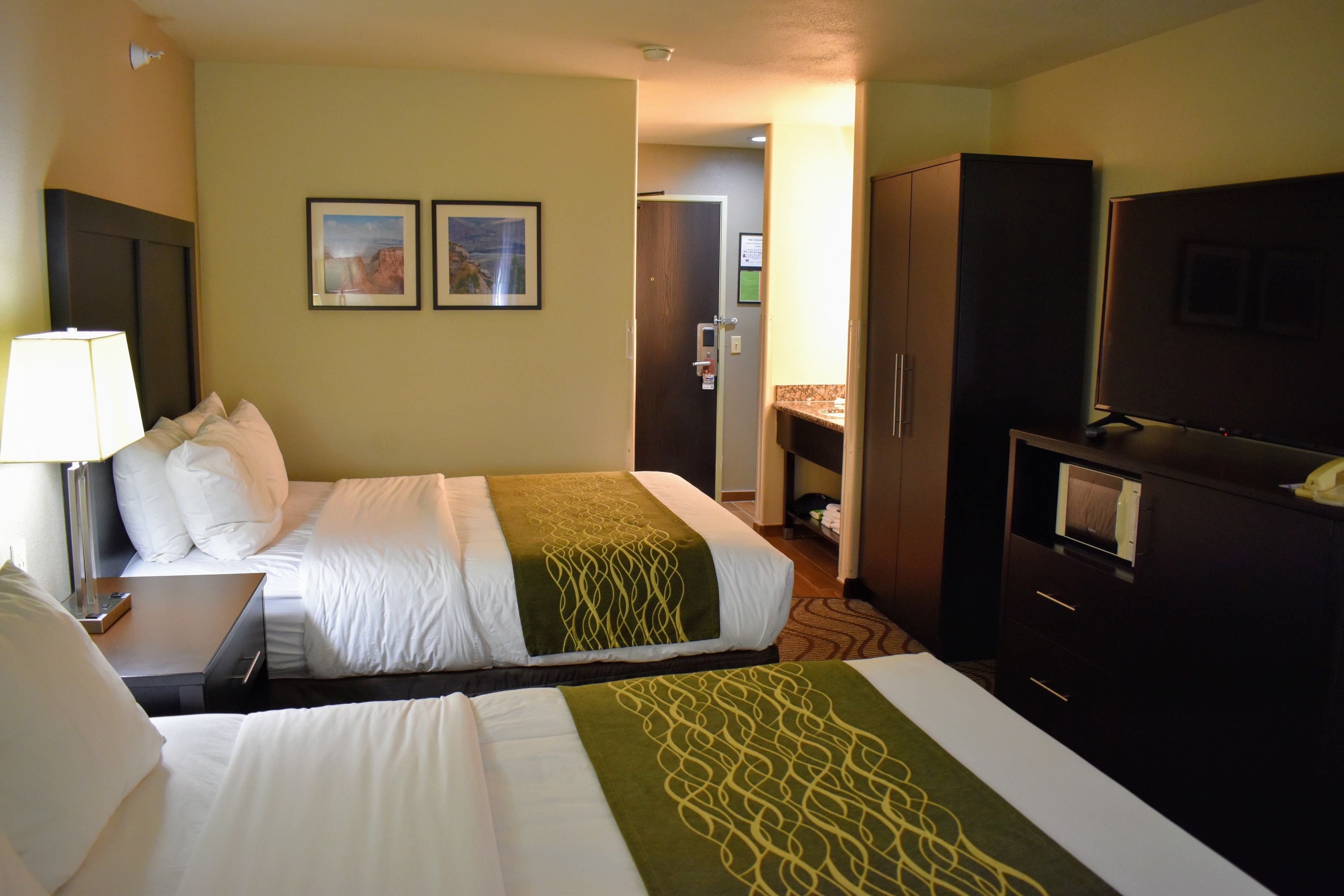 Una habitación de hotel con dos camas, un escritorio, una lámpara, un televisor y un armario.