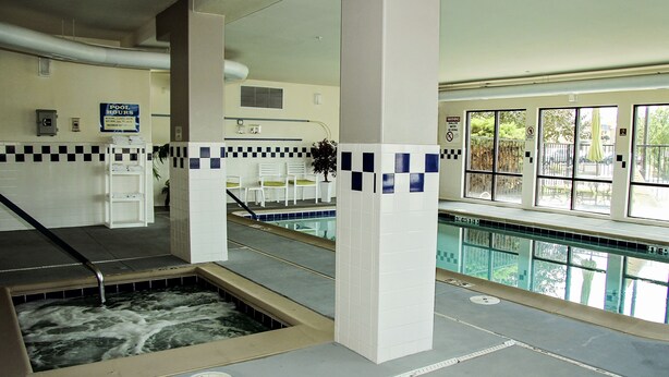 A pool area with a checkered tile border, a hot tub, and a sign indicating pool hours.