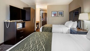A hotel room with two beds, a television, a desk with a lamp, and a minibar.