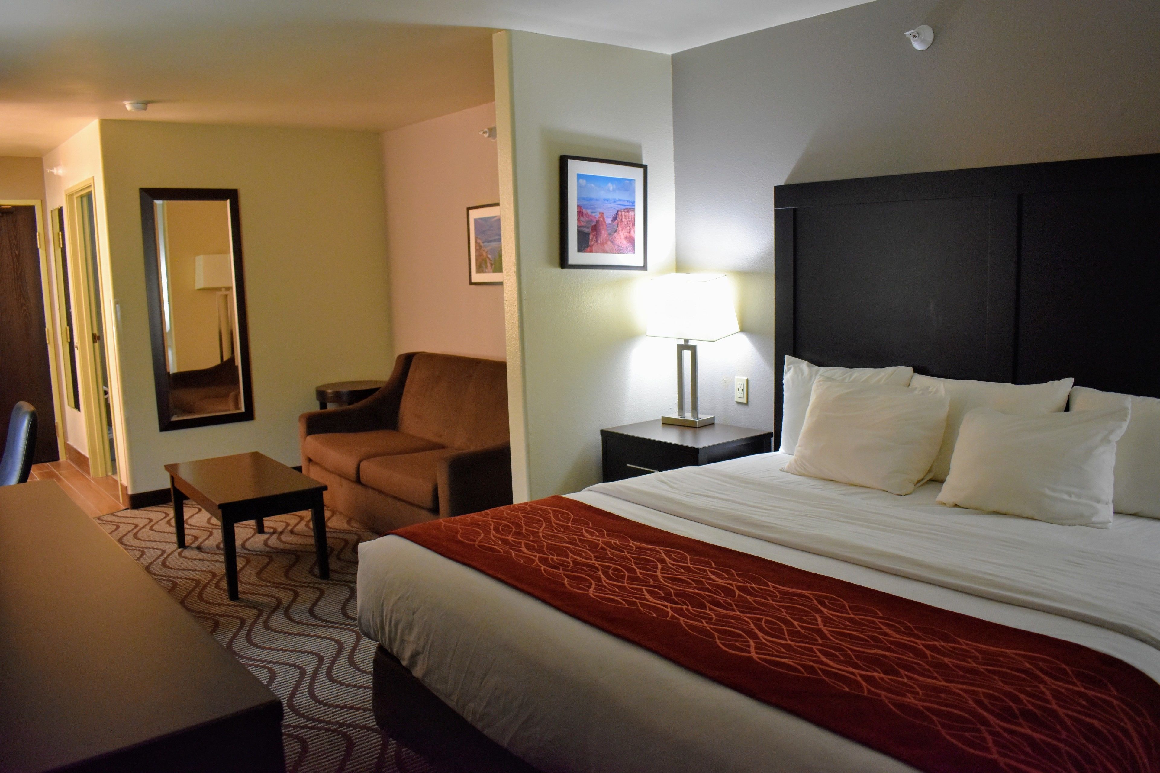A hotel room with a bed, a chair, a table, and a lamp.