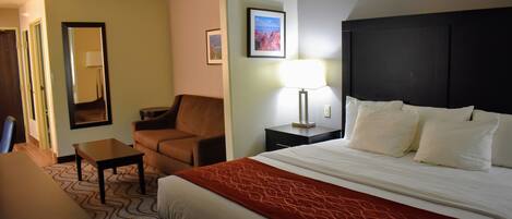 A hotel room with a bed, a chair, a table, and a lamp.