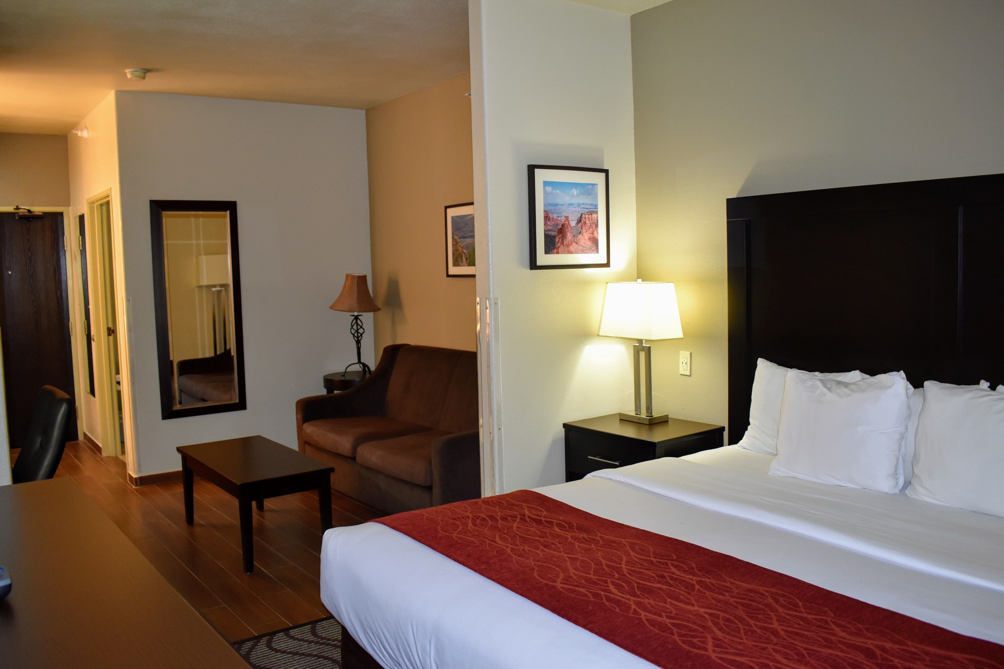 Una habitación de hotel con cama, escritorio, silla, lámpara y un cuadro en la pared.