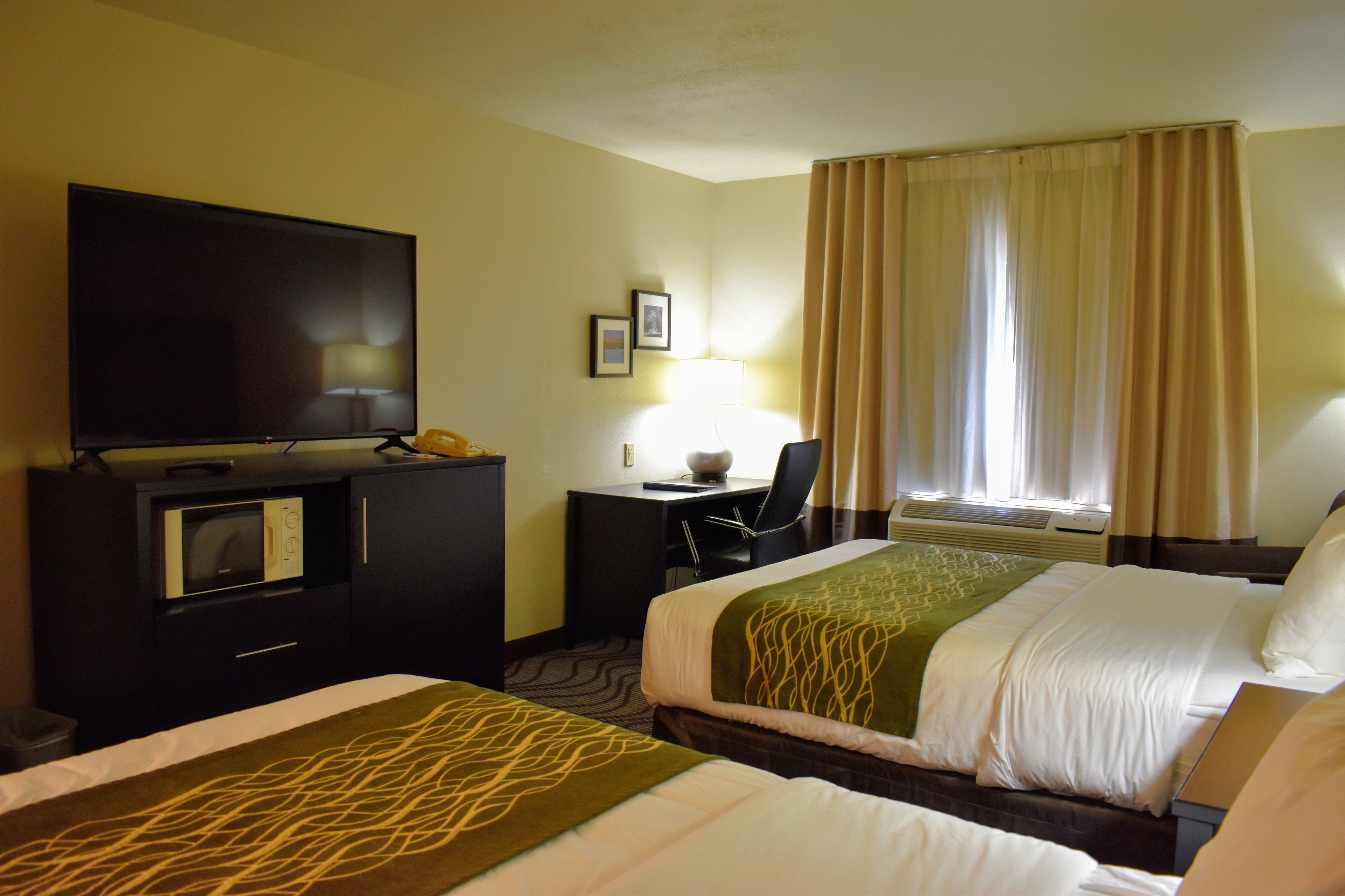 A hotel room with two beds, a desk with a computer, a TV, and a microwave.