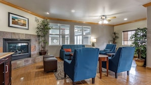 A living room with a fireplace, blue armchairs, a coffee table, and a TV. - Comfort Inn & Suites Fruita - Grand Junction (Fruita)