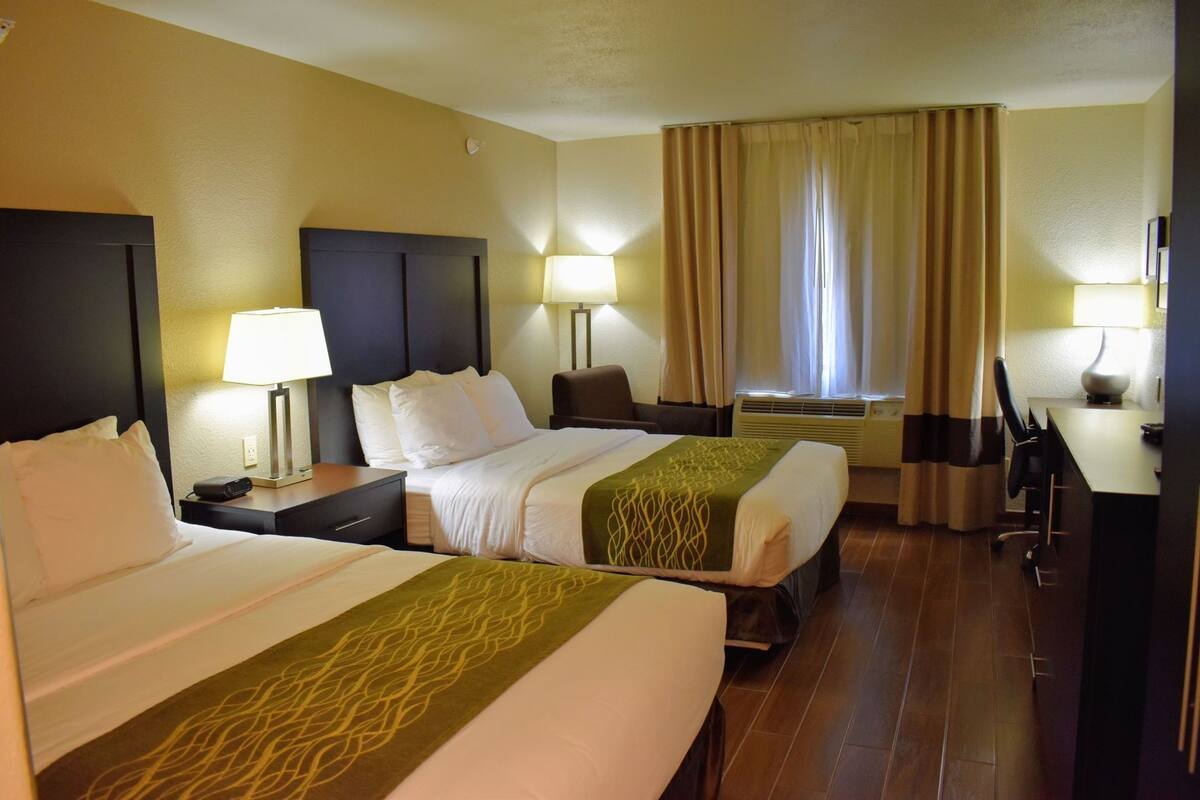 A hotel room with two beds, a desk, a chair, and a window with curtains.