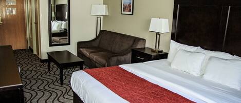 A hotel room with a large bed, a desk, a chair, a mirror, and a nightstand with lamps.