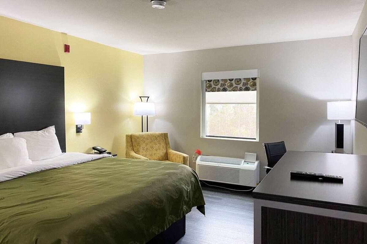 Une chambre d’hôtel équipée d’un lit, d’un bureau, d’une chaise, d’une fenêtre et d’un climatiseur fixé au mur.